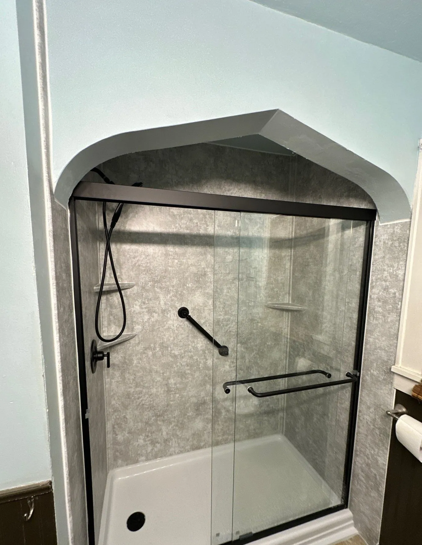 A finished walk-in shower with grey concrete-look walls, black-framed sliding glass doors and a low-threshold white base.